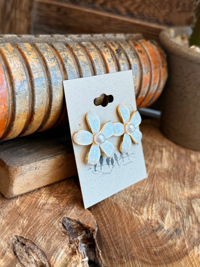 Angled shot of white pearl flower stud earrings with gold-tone posts and dangling black charms