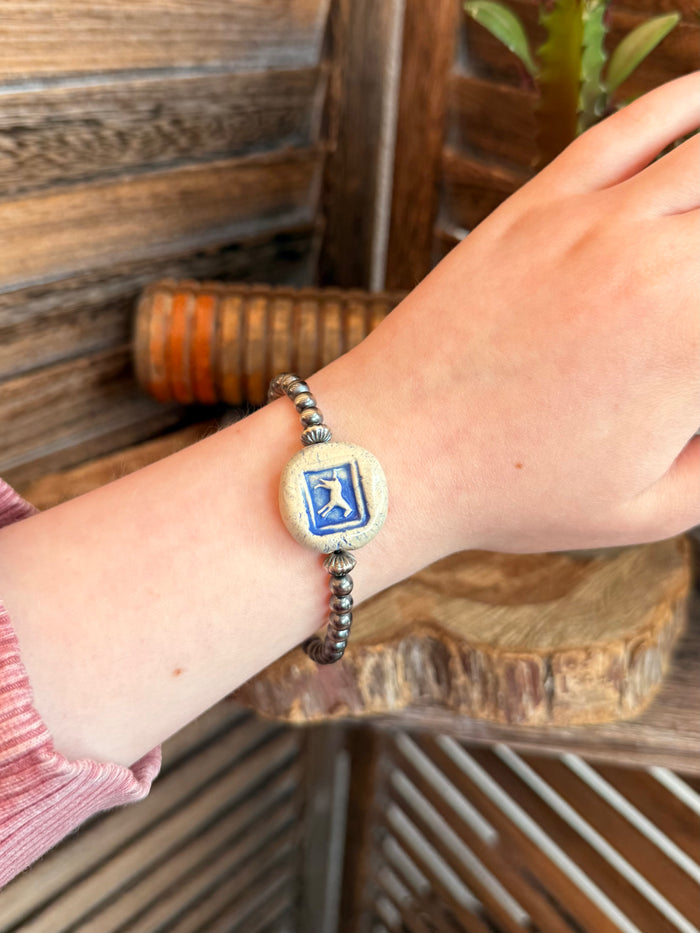 Stretchy bracelet on wrist with blue horse ceramic disc charm and silver-tone beads