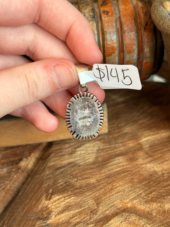 Small vintage pendant held in hand; oval silver-tone back with spiny rim