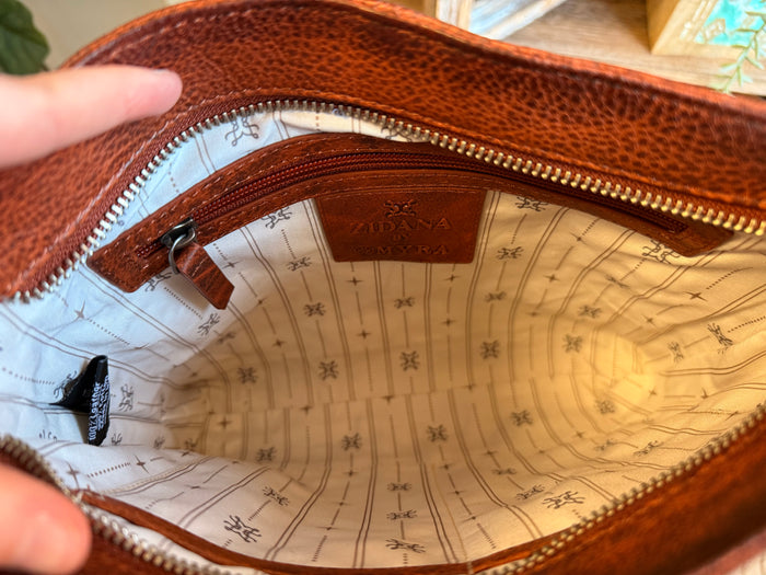 Opened rusty brown leather crossbody bag interior with patterned lining and top zipper