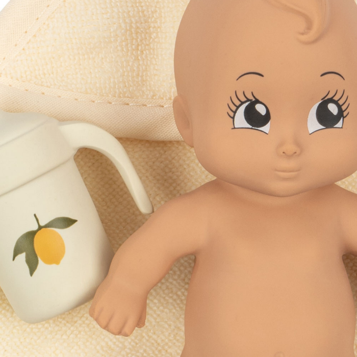 Baby doll with large eyes next to a white container with a lemon design on a beige background