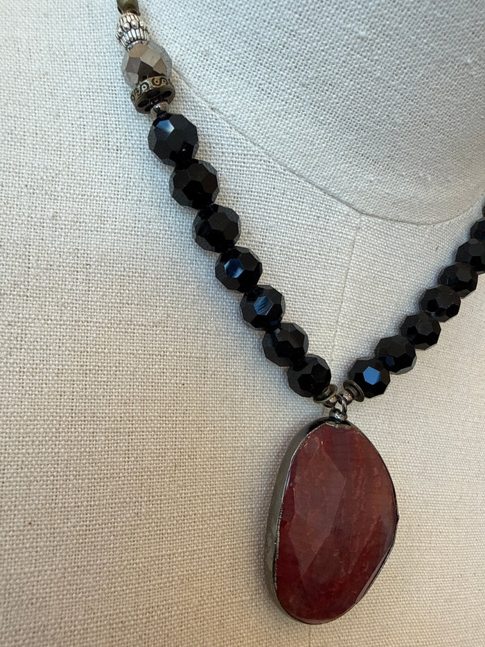 Close-up of black faceted bead necklace with red crystal drop pendant and metal bail