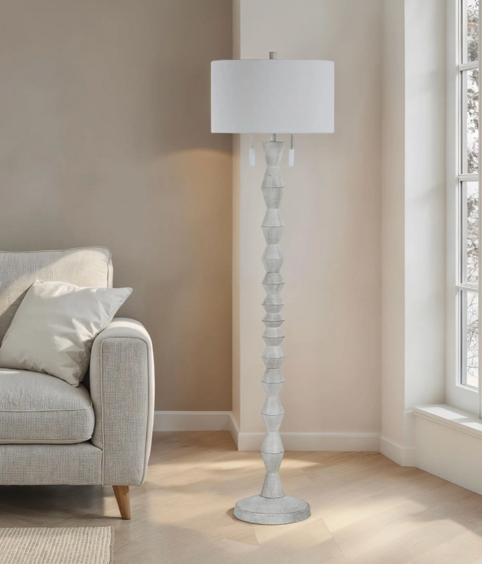 Decorative white floor lamp in a living room setting with a sofa and window.