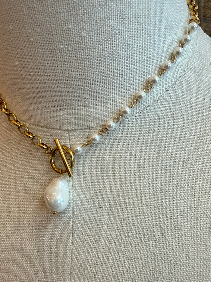 Gold chain necklace with toggle clasp and white pearl charm, close-up