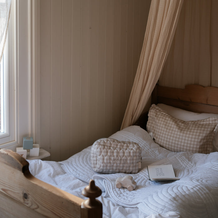Toiletry Pouch in Beige Gingham sitting on bed with Beige Gingham pillow.