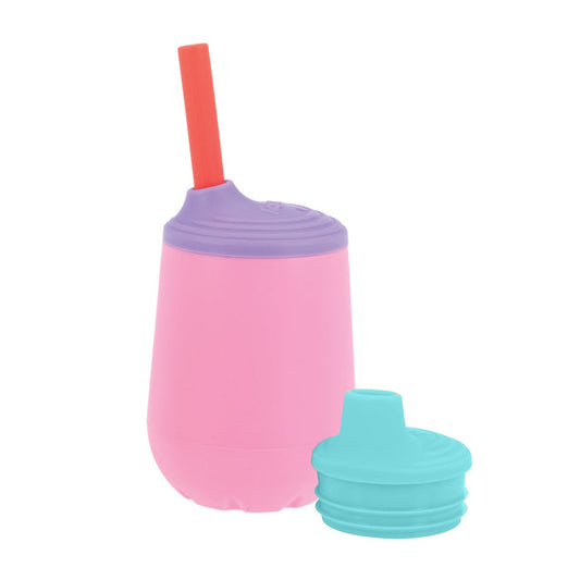 The Nuby US 3-Stage Training Cup Set | Pink features a pink silicone cup with a purple lid and red straw, shown upright next to an extra turquoise lid, illustrating its easy-transition design.
