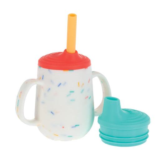 The Nuby US 3-Stage Training Cup Set with Handles | Confetti features a white cup with colorful specks, twin handles, a red lid with yellow no-spill straw, and a teal silicone spout lid shown beside it.