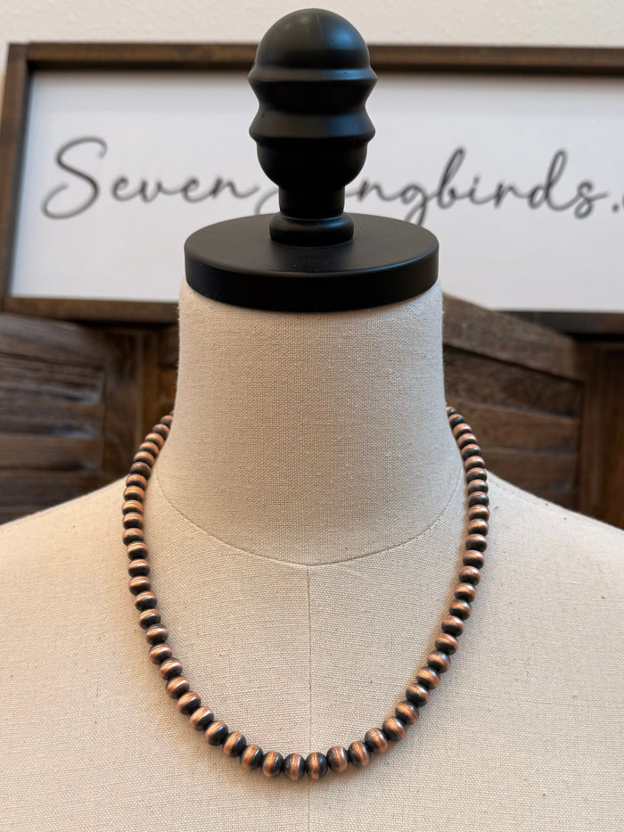 Copper bead necklace on a mannequin, round beads with dark accents and copper shine