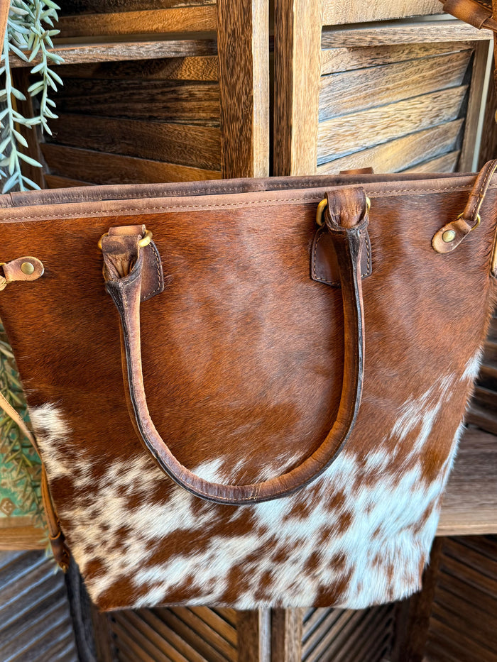 Brown-and-white cowhide crossbody purse with leather handles and adjustable strap