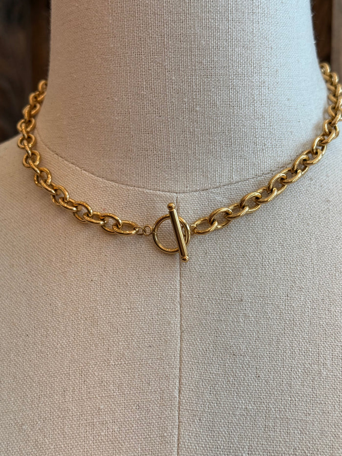 Gold chain necklace detail: V toggle clasp with bar, close-up on mannequin neck