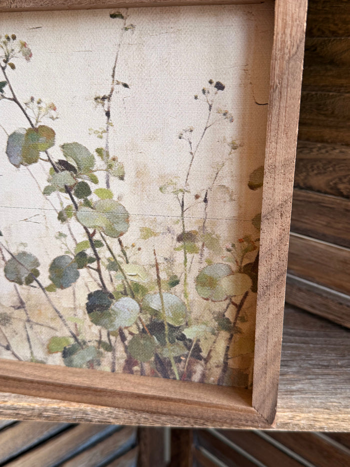 Close-up of wood-framed botanical leaf landscape artwork with green foliage