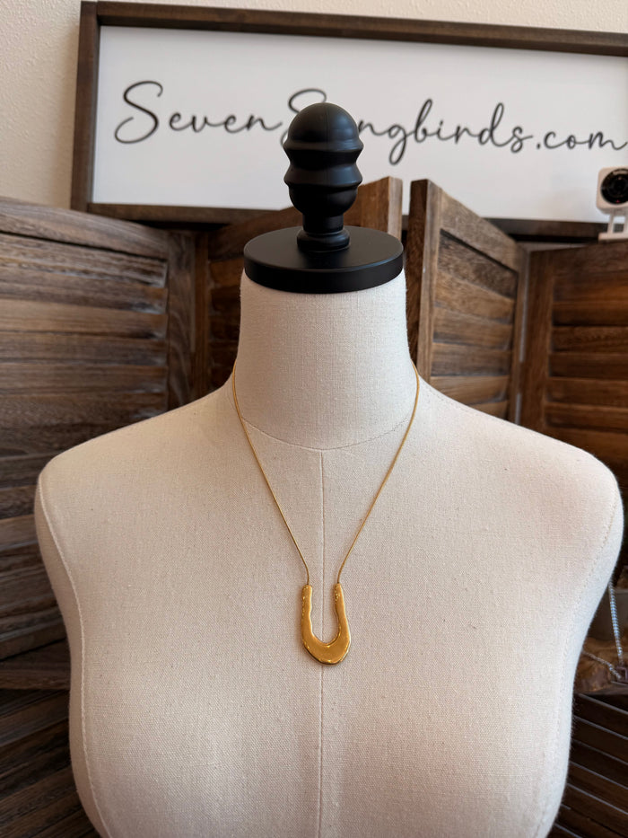 Gold wavy U-shaped stainless steel necklace with double-prong pendant, on mannequin