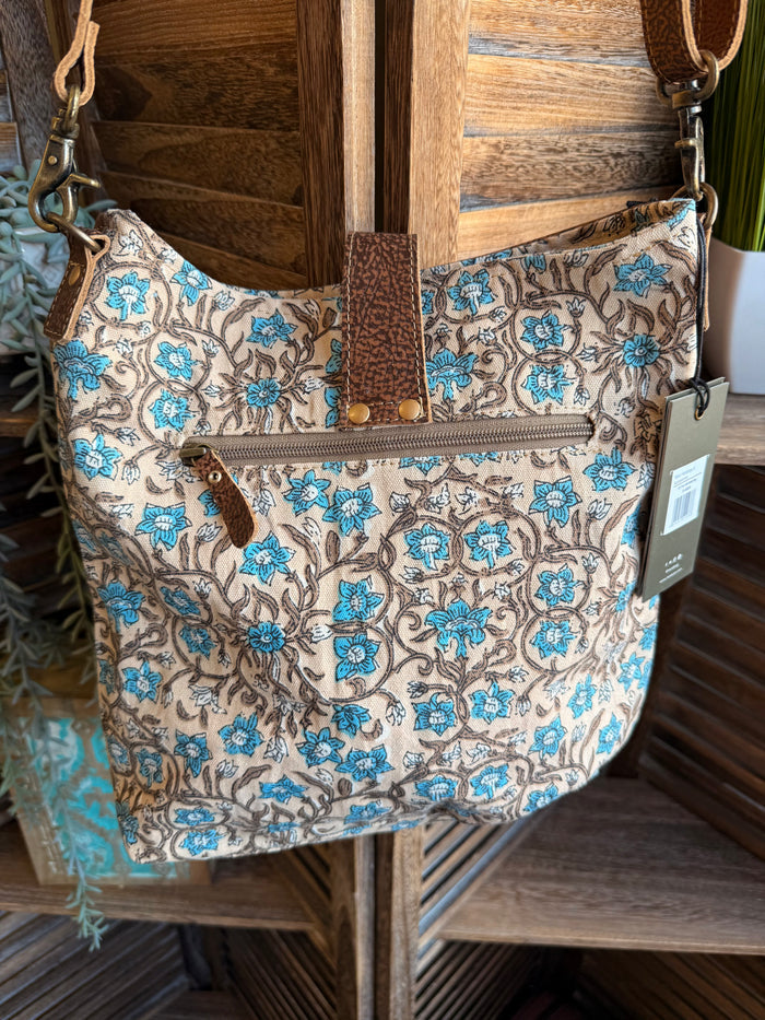 Turquoise floral canvas tote with brown leather handle straps and front zip pocket
