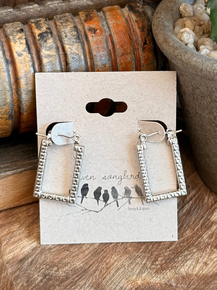 Pair of silver textured trapezoid stud earrings with dangling square frames on display card.