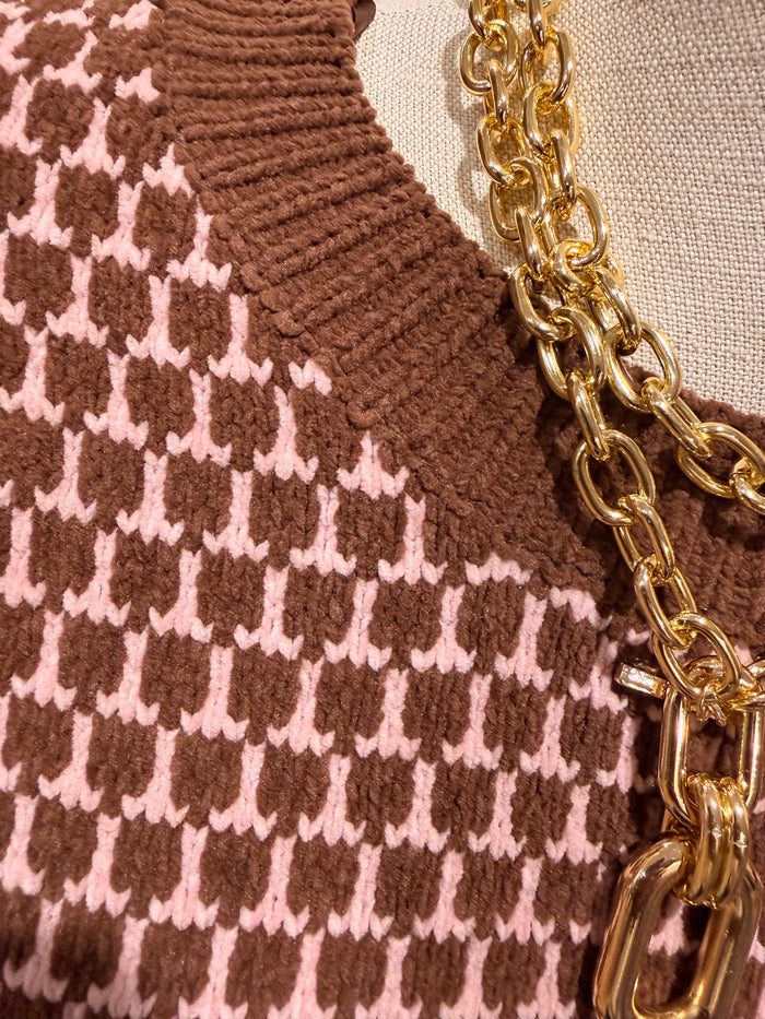 Close-up of a brown and pink knit sweater with a gold chain detail on a beige fabric mannequin.