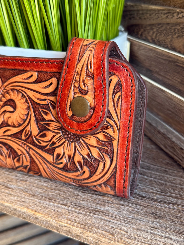 Tooled leather clutch wallet side view with round snap stud and floral embossing.