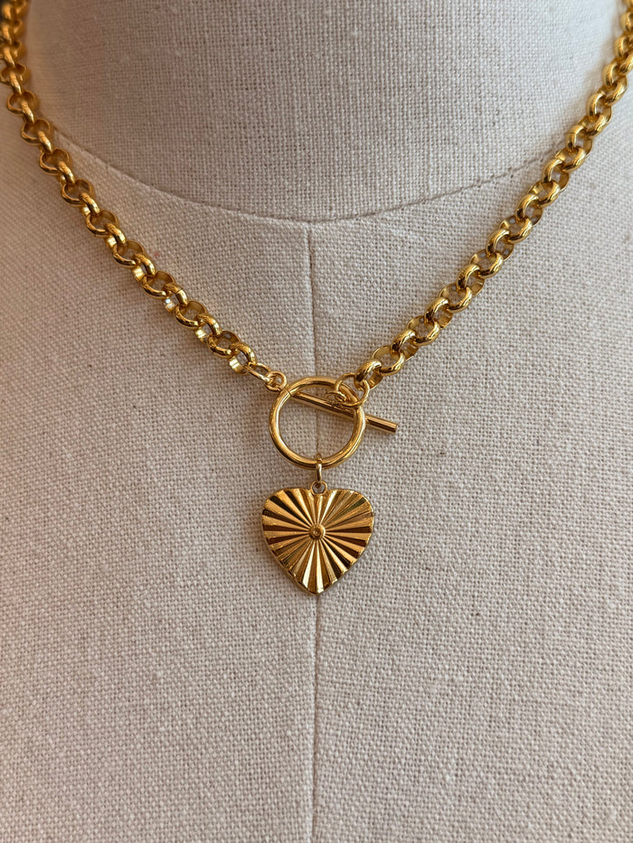 Gold-tone chain necklace close-up: toggle clasp bar and sunburst heart charm