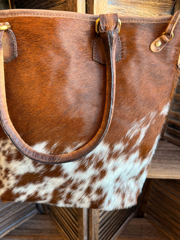 Cowhide crossbody purse close-up: brown leather trim with white speckled body