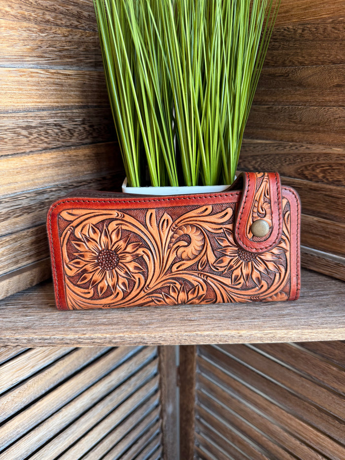 Tooled leather clutch wallet with floral embossing and snap closure, orange-brown.