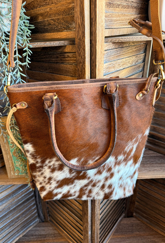 Cowhide crossbody purse with brown hide and white speckled panels, top U-handle