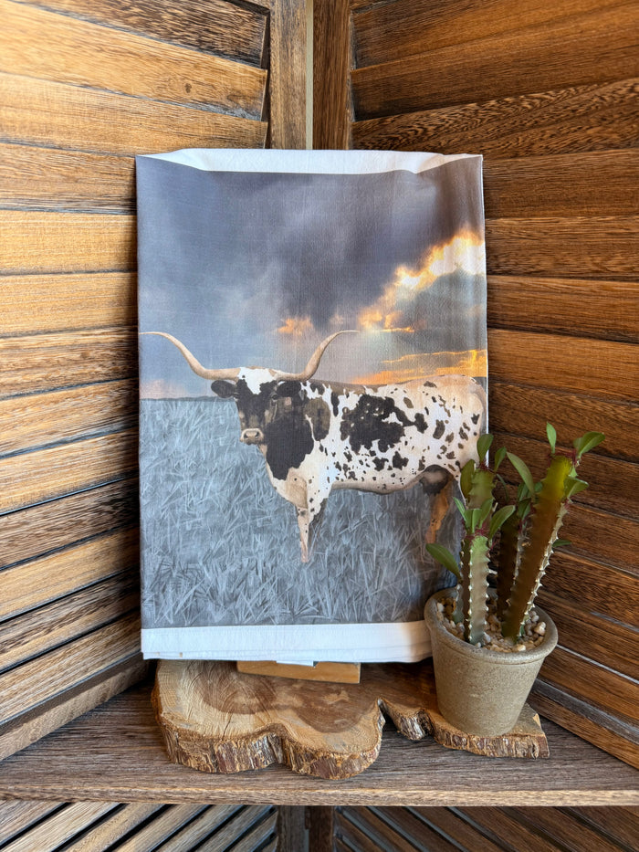 Watercolor tea towel with black-and-white longhorn over cloudy blue sky