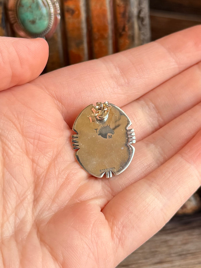 Silver stud earring back with stamped marks and small loop, shown on hand