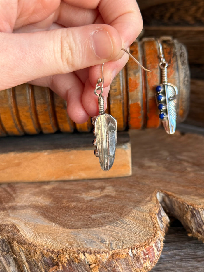 Silver lapis feather fishhook earring held by hand with blue bead dangle