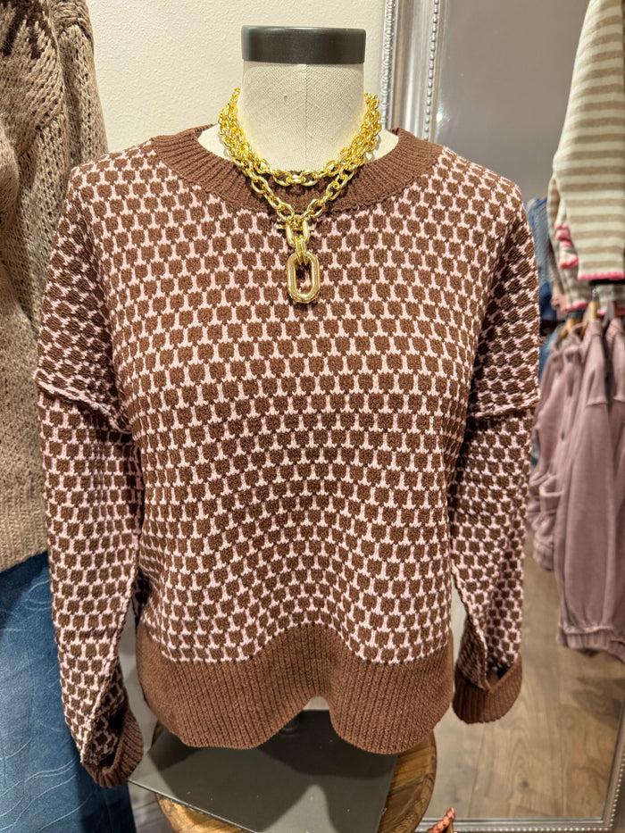 A brown and beige patterned knit sweater displayed on a mannequin torso, styled with a chunky gold chain necklace in a retail setting.