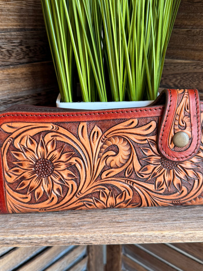 Tooled leather wallet close-up with floral pattern and snap strap, orange-brown.