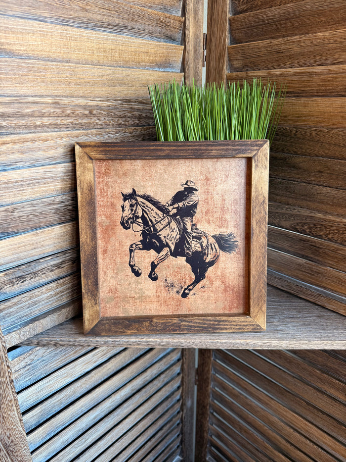 Framed cowboy riding artwork with black horse and rider illustration, rustic wood-look frame