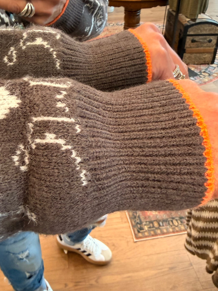 Brown knit sweater sleeve close-up with cream paisley motif and orange trim
