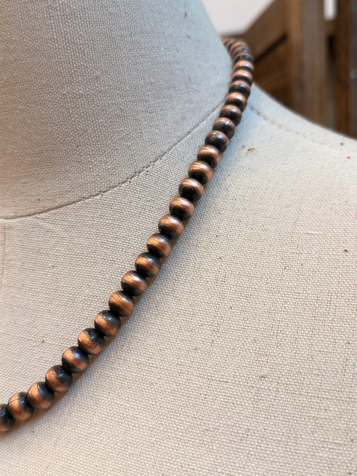 Close-up of copper-tone round beads with dark accents along the necklace strand