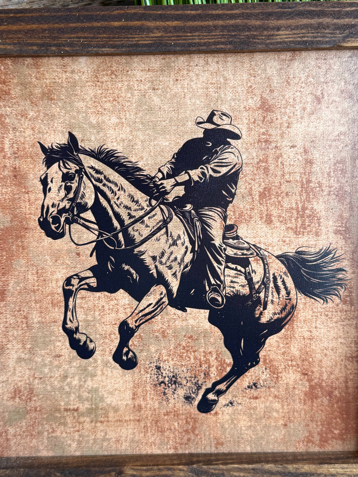 Close-up of framed cowboy riding horse artwork with black illustration on textured beige background