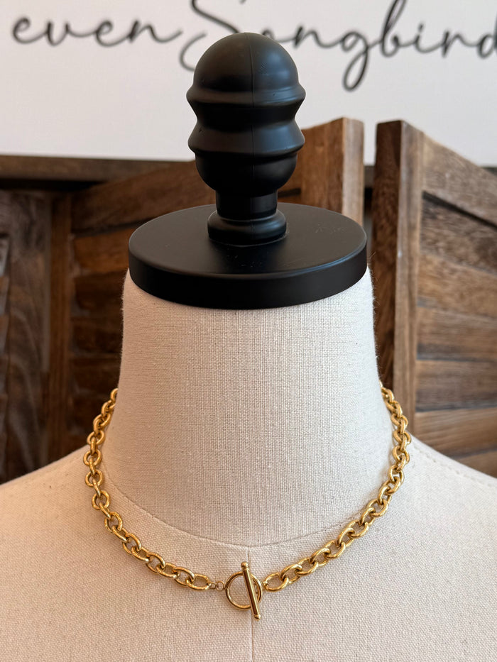 Gold chain necklace with V-shaped toggle clasp at center, front view on mannequin