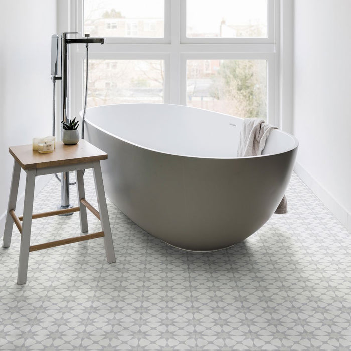 Freestanding bathtub in a bright bathroom with white and grey patterned floor tiles.
