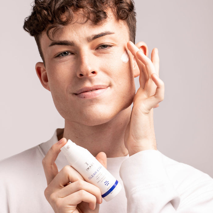 Young man applying CLEAR CELL clarifying repair crème | IMAGE Skincare to his cheek, demonstrating skincare use in a wellness routine.