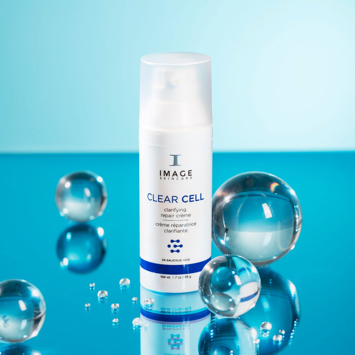 CLEAR CELL clarifying repair crème | IMAGE Skincare bottle surrounded by clear glass spheres on a reflective blue surface, highlighting skincare and wellness themes.