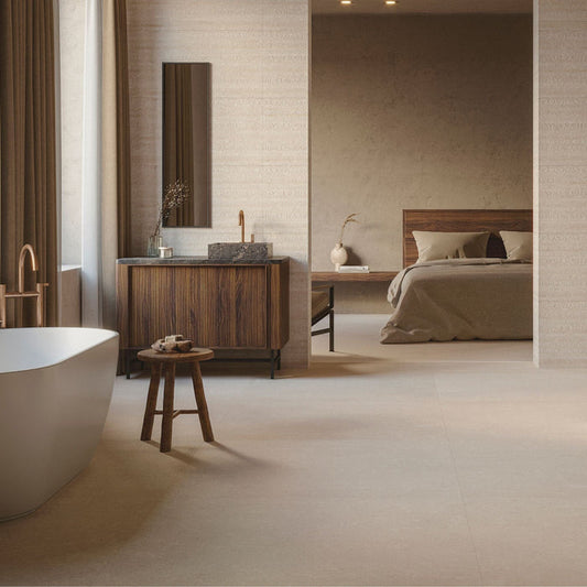 Bathroom with freestanding bathtub, wooden vanity unit, beige stone effect tiles looking into a bedroom.