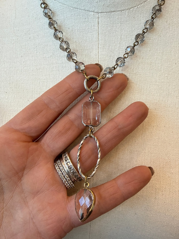 Crystal teardrop charm necklace on silver-toned chain, held in hand