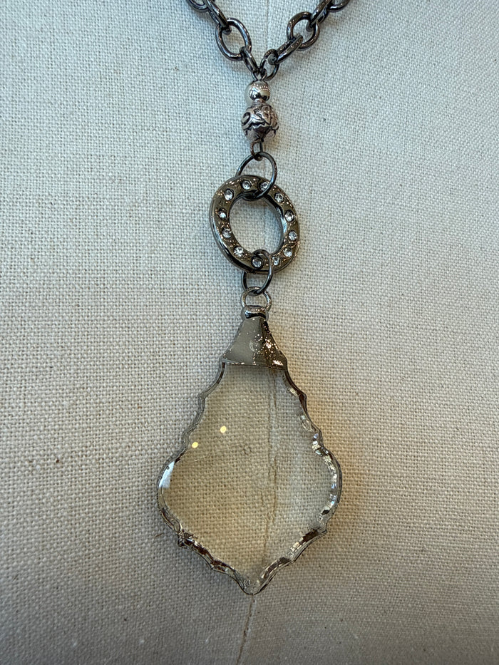 Silver-tone necklace with circular bezel charm and faceted teardrop crystal pendant.