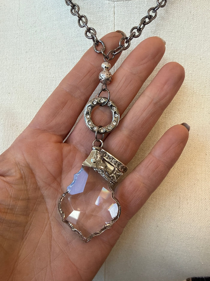 Silver-tone crystal pendant necklace held in hand, showing faceted teardrop stone.