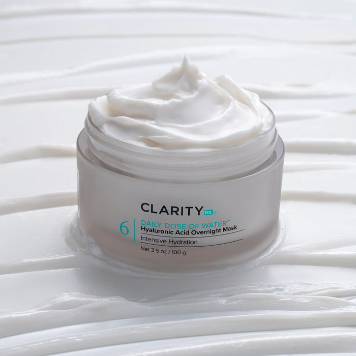 Open jar of creamy white skincare product labeled Daily Dose of Water™ Hyaluronic Acid Overnight Mask | ClarityRx, placed on textured white surface with smooth cream swirls.