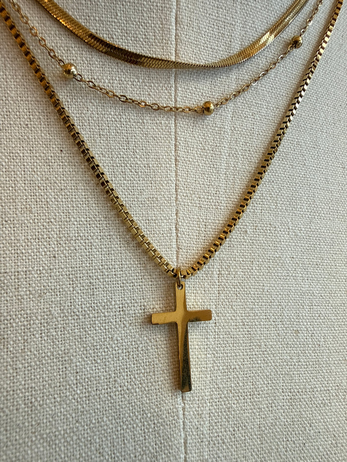 Gold cross pendant on triple-layer necklace, fine chain with small round beads