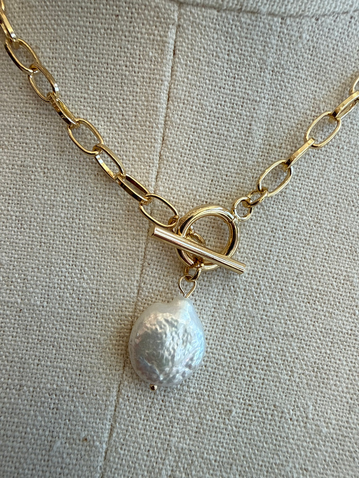 Gold chain necklace close-up: toggle clasp bar with white pearl drop