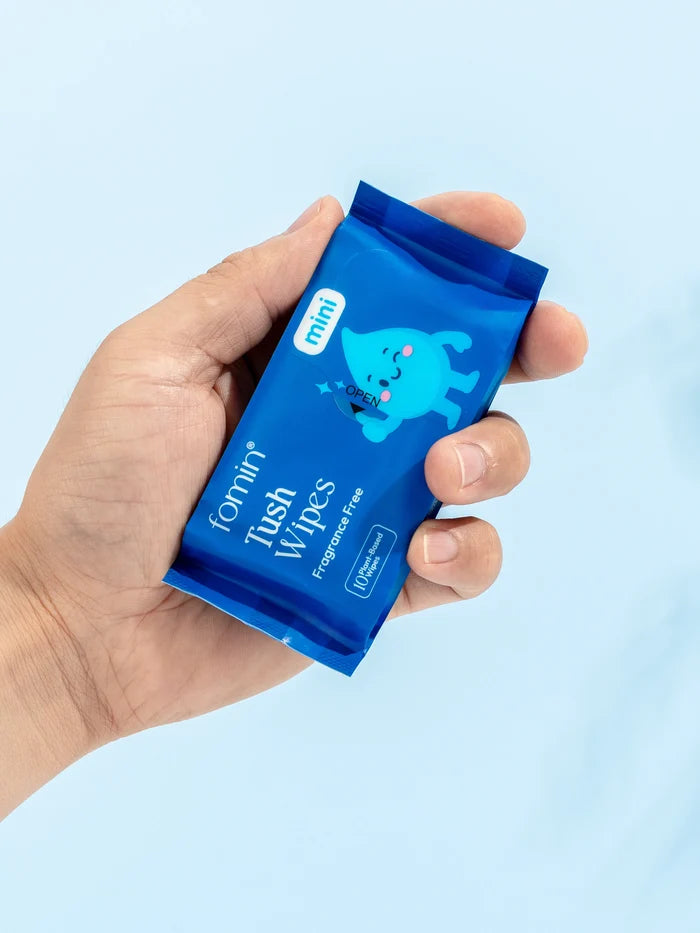 Hand holding a blue packet of Tush Wipes with a light blue background