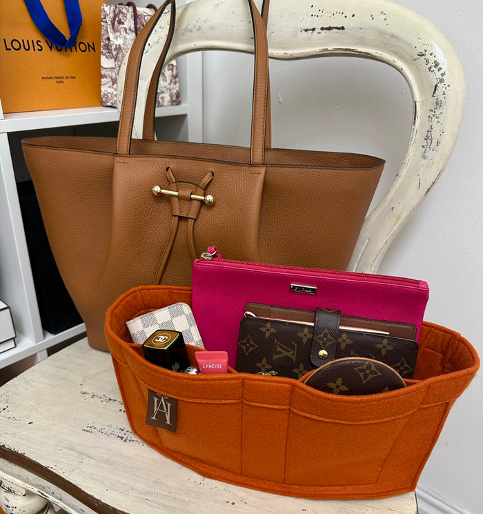 Tan tote bag behind an orange felt handbag organiser filled with a pink pouch, wallet and cosmetics.