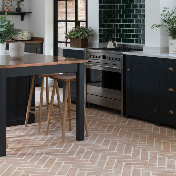 Modern kitchen with black island, oven, and terracotta floor.