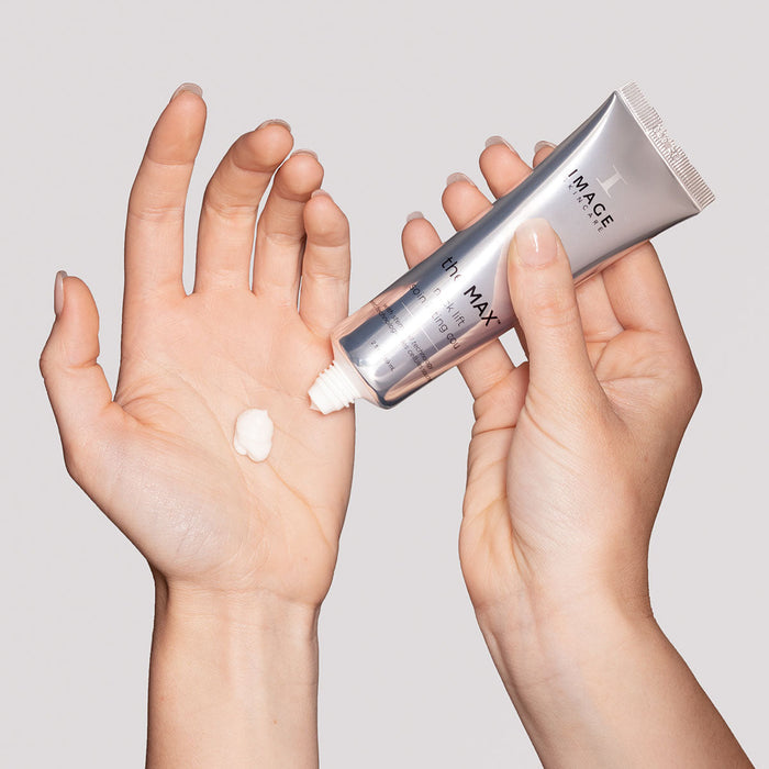 Person squeezing a small amount of MAX™ neck lift | IMAGE Skincare cream onto the palm, showcasing a smooth white skincare product.