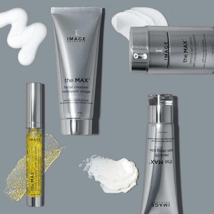 Collection of skincare products from the MAX™ neck lift | IMAGE Skincare line displayed on a gray surface with cream and serum textures around the bottles and tubes.