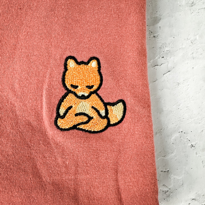 Close-up of a soft pink fabric featuring an embroidered meditating fox patch on the Meditating Fox Comfy Tee | Lucky Owl.